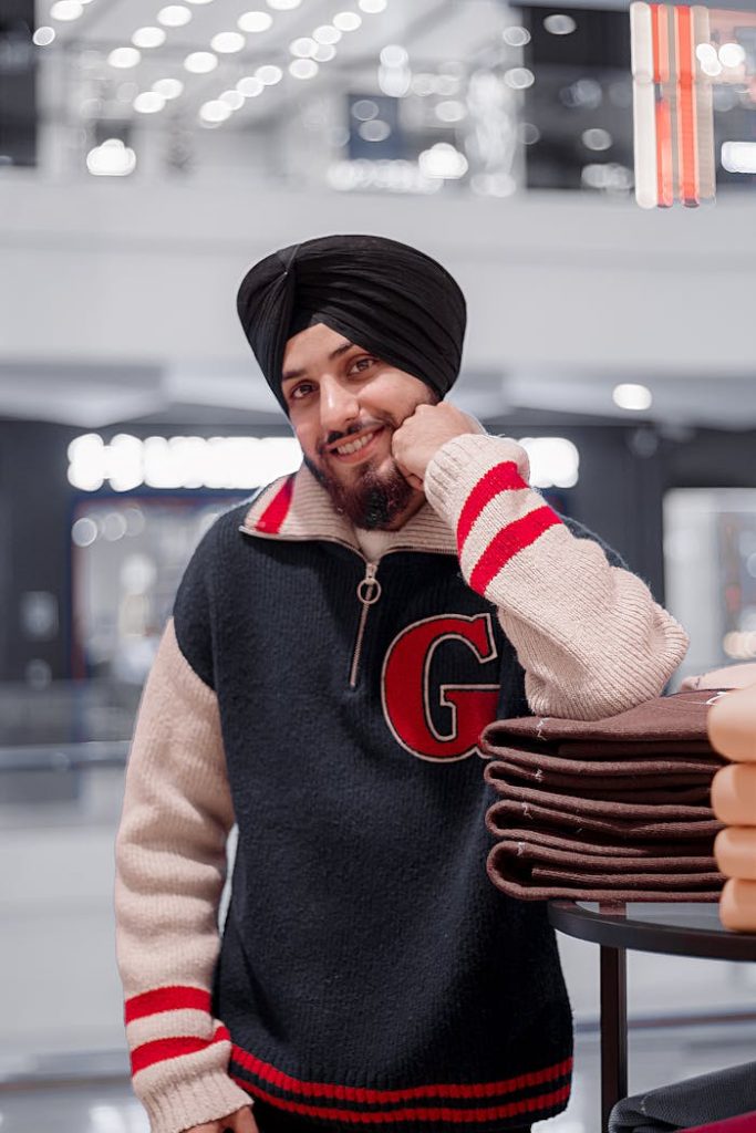 Smiling man in a sweater and turban posing indoors in a New Delhi mall.